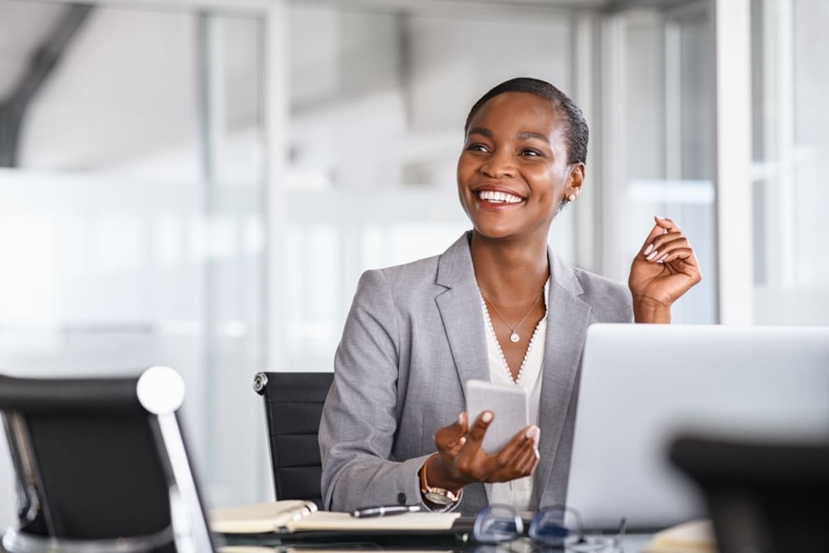 A happy business woman at her desk and holding her phone.