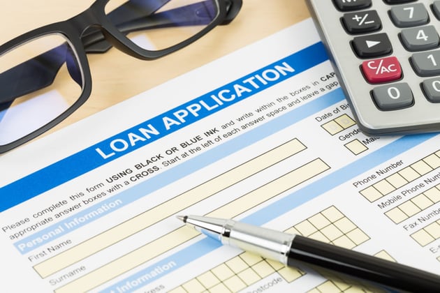 A document labeled loan application next to a pen, glasses, and a calculator