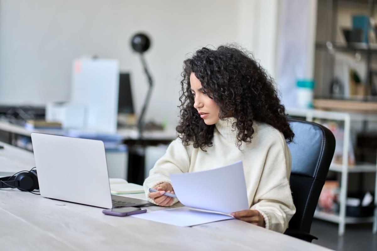 A woman reviewing a document and looking at her computer